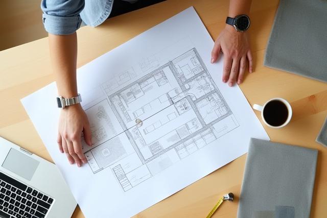 Diseñadora de interiores revisando planos sobre una mesa de madera, con muestras de tela y un ordenador portatil.